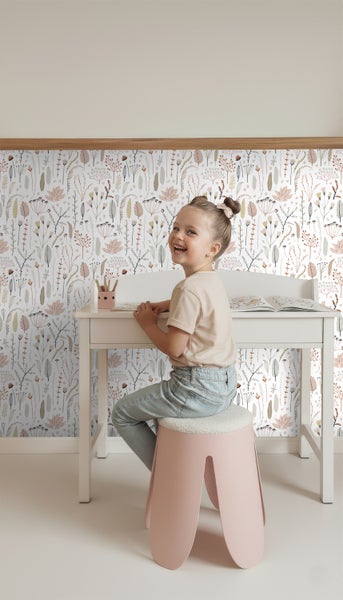 Mädchen sitzt an einem weißen Kinderschreibtisch vor einer floralen Tapete