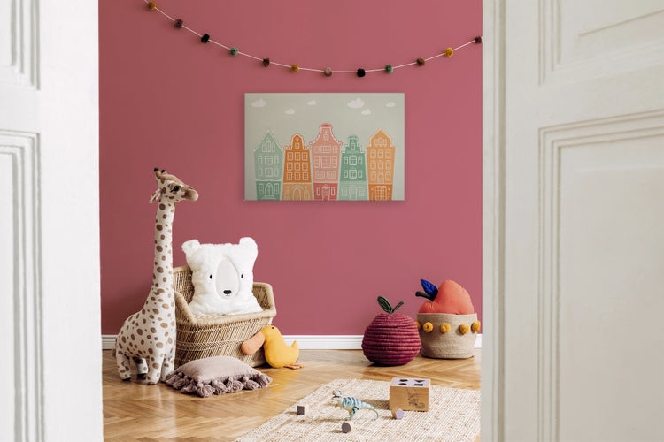 Ein Kinderzimmer mit einem Wandbild im Stil niederländischer Giebelhäuser, Giraffenstofftier, Korb, Spielzeug und bunter Wimpelkette.