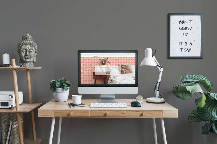 Organisierter, moderner Arbeitsplatz mit Holzschreibtisch, Computer, weißer Schreibtischlampe, Zimmerpflanzen und Dekoartikeln wie einem Buddhakopf.