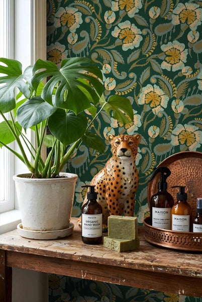 Rustikaler Holztisch vor floraler Tapete mit Monstera im Topf, Leopardenfigur, Seifenstücken und Pflegeprodukten auf einem Metalltablett.