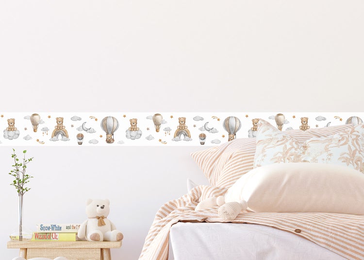 Hell gestaltetes Kinderzimmer mit einer Bordüre mit Teddybär- und Heißluftballon-Motiven über einem Bett mit gestreifter Bettwäsche.