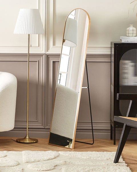 Stehspiegel mit Holzrahmen und schwarzem Metallfuß in einem Wohnzimmer mit Lampe, Teppich und Schrank