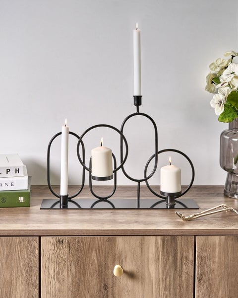 Kerzenständer mit geometrischen Formen und brennenden Kerzen auf einem Holzschrank