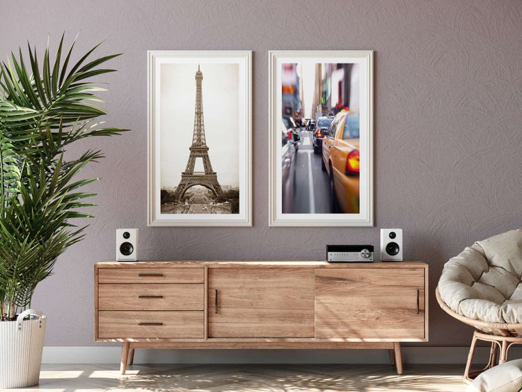 Modernes, hell eingerichtetes Wohnzimmer mit Sideboard aus Holz, zwei gerahmten Bildern vom Eiffelturm und einer Straßenszene sowie Zimmerpflanze.