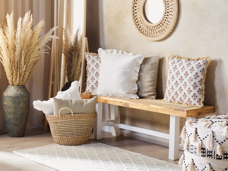 Dekoratives Interieur mit Bank, Kissen, Vase mit Ziergras, Korb und rundem Spiegel