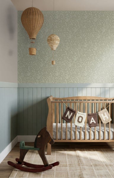 Helles, organisiertes Kinderzimmer mit floral gemusterter Tapete, Holz-Gitterbett mit Namenskette, Schaukelpferd und Wandpaneelen.