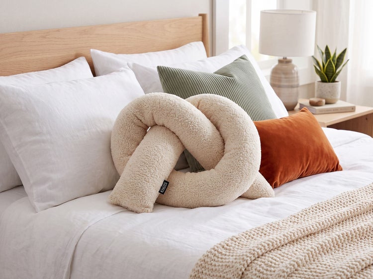 Dekoratives Knotenkissen aus kuscheligem Teddyfell auf einem modern eingerichteten Bett mit verschiedenen Zierkissen.