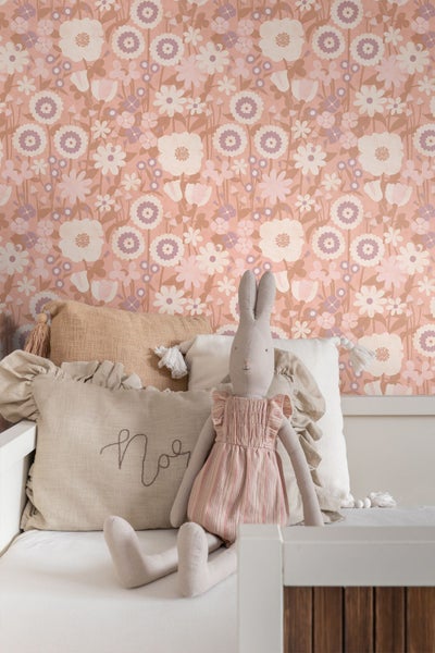 Vliestapete mit floralem Retromuster in einem Kinderzimmer hinter einem Bett mit Dekokissen und Stoffhasen.
