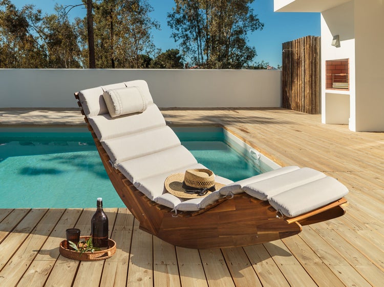 Holzliege mit Polsterauflage am Pool mit Getränken und einem Hut