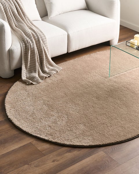 Runder Hochflor-Teppich auf Holzfußboden in einem hellen Wohnzimmer mit weißem Sofa und Glastisch.