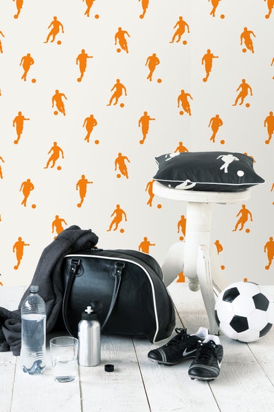 Szene mit Sporttasche, Fußball, Fußballschuhen, Getränkeflaschen und Kissen auf einem Hocker vor einer Fußballtapete.