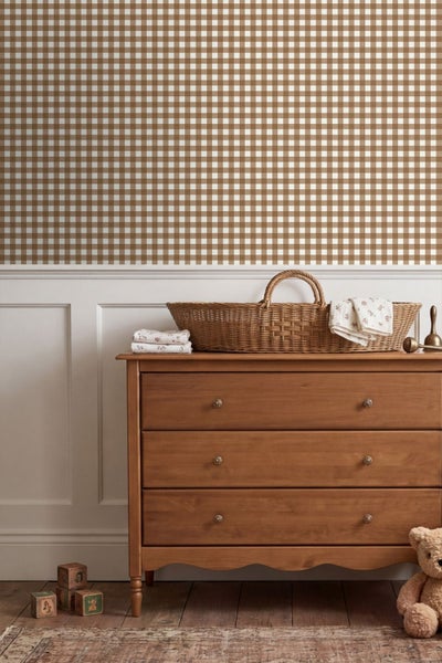 Kinderzimmer mit braun-weiss karierter Tapete, weisser Wandvertaefelung und einer Holzkommode mit Weidenkorb.