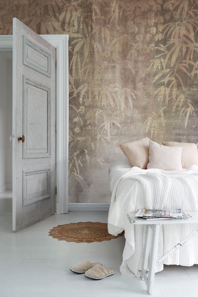 Heller Raum mit Bett, gemusterter Tapete, offen stehender Tür und kleinem Tisch