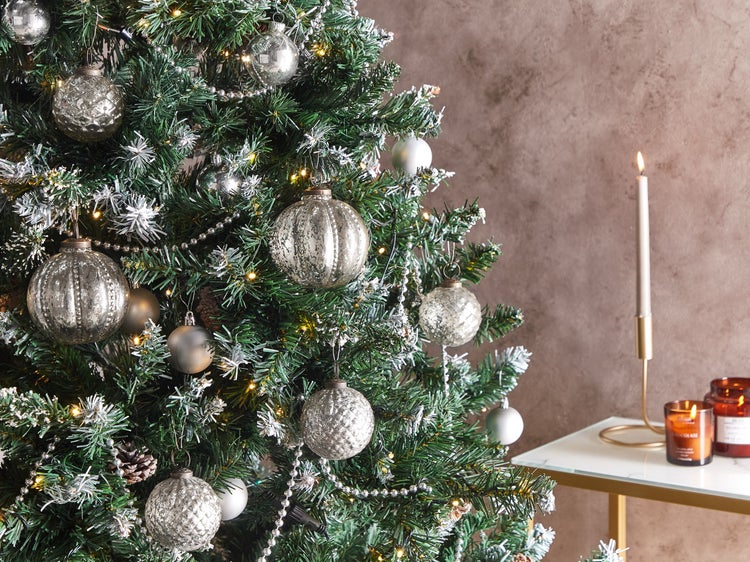 Geschmückter Weihnachtsbaum mit Kugeln und Beleuchtung neben einem Tisch mit Kerzen