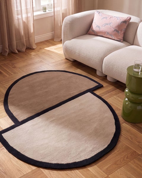 Moderner runder Teppich mit geometrischem Design in einer hellen Wohnzimmereinrichtung mit Sofa und Holzboden.