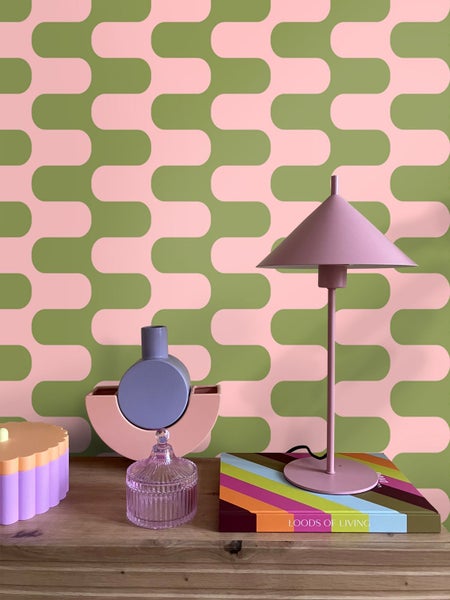 Dekorative Tischszene mit Lampe, Vase und Buch auf einem Holztisch vor einer gemusterten Tapete.