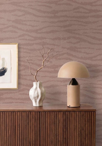 Wand mit Tapete mit wellenförmigem Muster über einer Holzkommode mit Tischlampe und Vase in einem modern eingerichteten Wohnbereich.