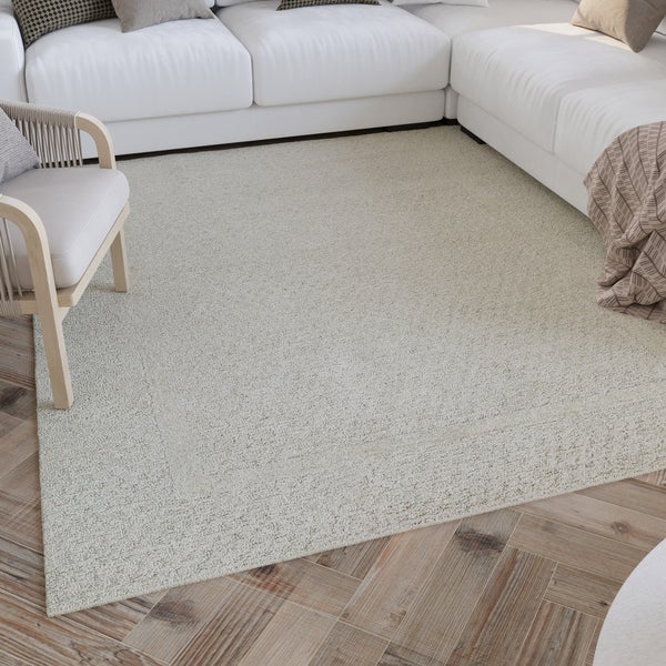 Strukturierter rechteckiger Teppich in einem hellen Wohnzimmer auf einem Fischgrät-Holzfußboden mit weißem Sofa und Holzarmsessel.