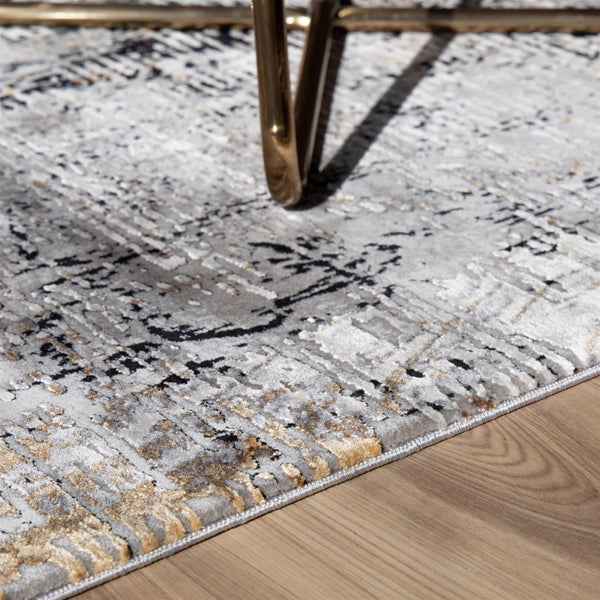 Moderner Teppich mit abstraktem Muster in Grau und Gold auf einem Holzboden.