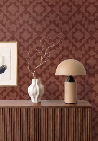 Tapete mit geometrischem Muster auf einer Wand hinter einem Sideboard mit Tischlampe und Vase in einem modern eingerichteten Raum.