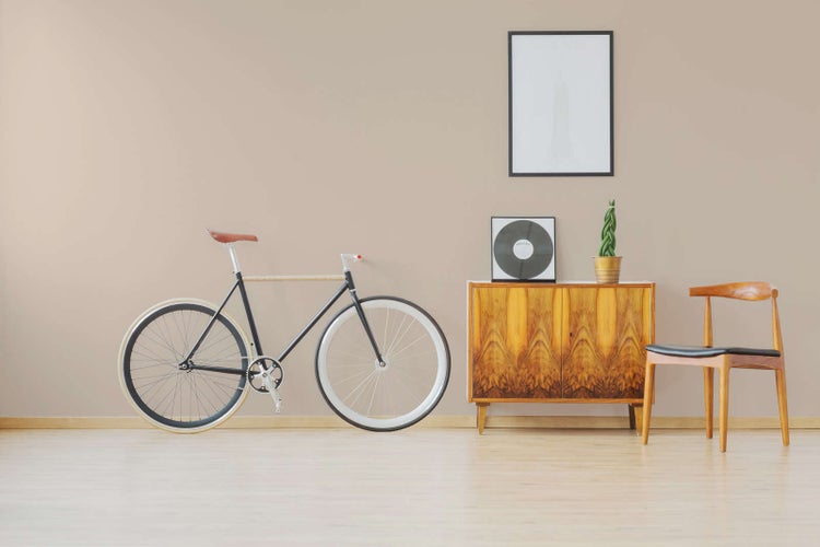 Modernes Zimmer mit beiger Wand, hellem Holzboden, einem Fahrrad, einer Holzkommode und einem Holzstuhl.