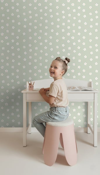 Mädchen sitzt an einem Kinderschreibtisch vor einer Wand mit Blumenmustertapete