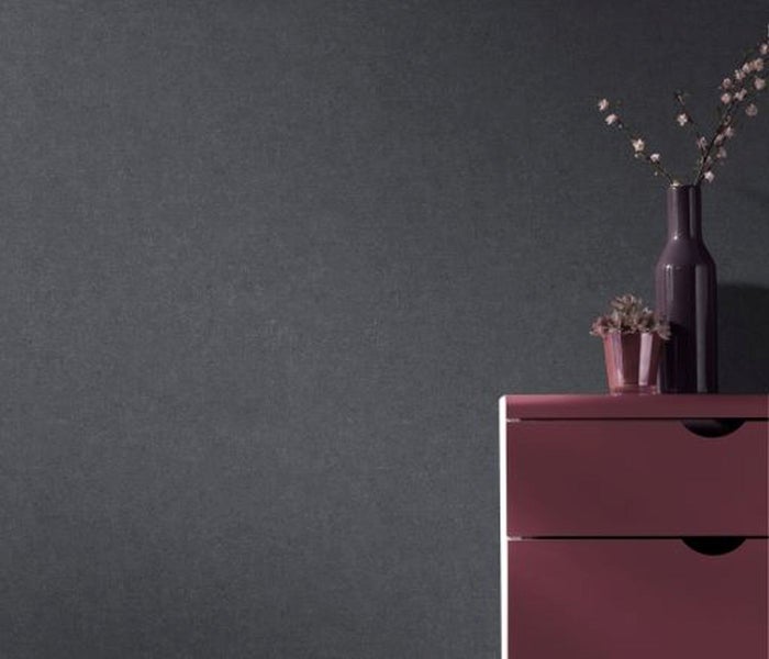 Strukturierte, dunkle Wand mit Kommode, Blumenvase und Pflanze.