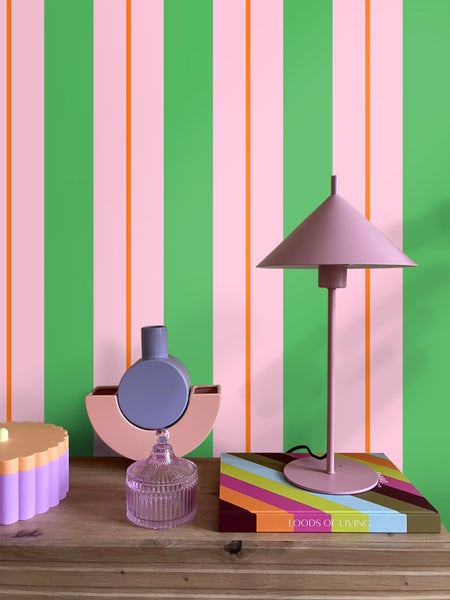 Dekorative Anordnung mit Lampe, Dose und Vasen auf einem Holzschrank vor einer gestreiften Wand.