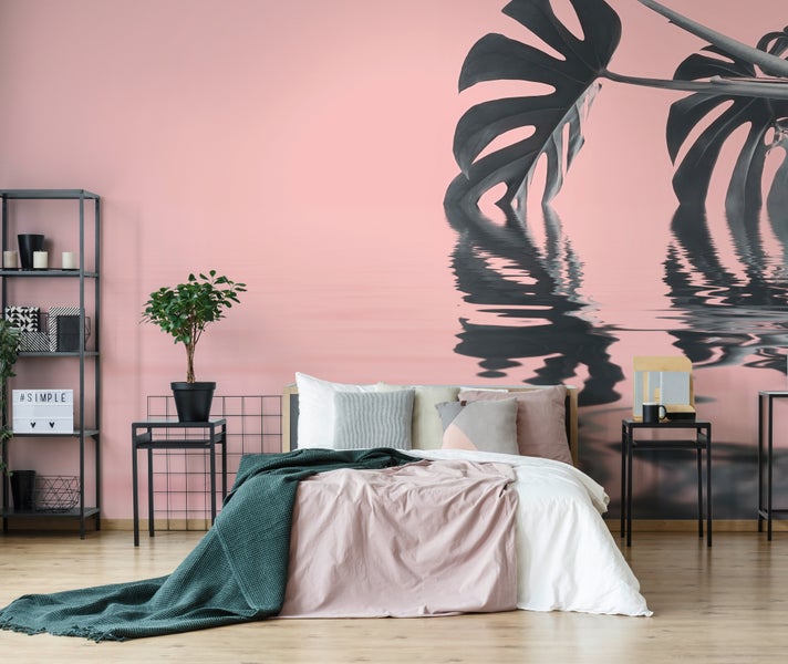 Fototapete mit Monstera-Blatt und Spiegelung im Wasser im modernen Schlafzimmer mit Bett und schwarzen Metallmöbeln.