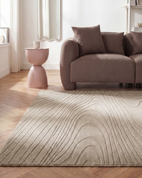 Modernes Wohnzimmer mit rechteckigem beigefarbenem Teppich mit wellenförmigem Muster auf Parkettboden neben einem braunen Sofa.