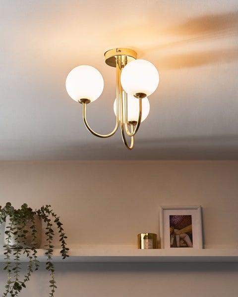 Dreiflammige Deckenleuchte aus goldfarbenem Metall mit weißen Glaskugeln in einem hellen Raum über einem Regal mit Dekoration.