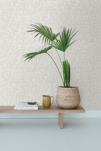 Dekorative Wand mit Textiltapete, Zimmerpflanze im Korb, Krug und Bücher auf einem Regal