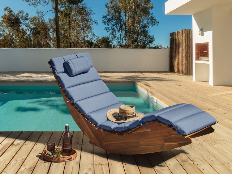 Geschwungene Gartenliege aus Holz mit blauer Polsterauflage auf einer Holzterrasse am Pool.