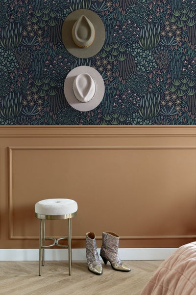 Vliestapete mit botanischem Muster über Wandvertäfelung, Hocker mit Samtbezug, Glitzerstiefel und dekorative Hüte an der Wand.