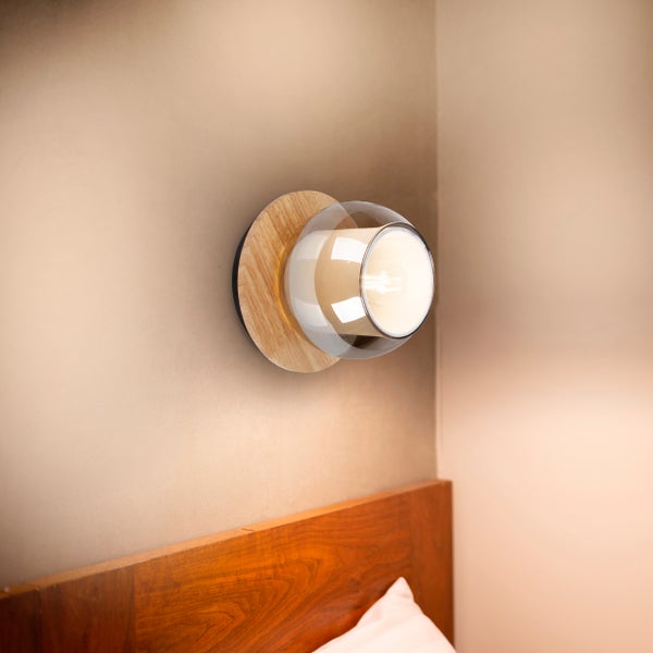 Wandleuchte mit hölzerner Rückwand und kugelförmigem Glasschirm im Schlafzimmer