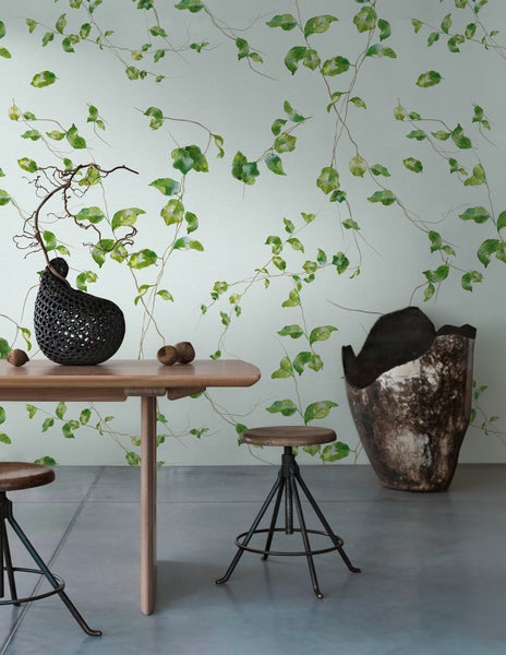 Vliestapete mit Blättermuster und Ranken in einem modern eingerichteten Raum mit Holztisch und Hockern.