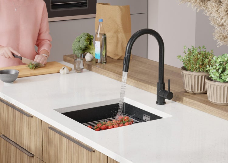 Küchenszene mit Spüle, Armatur, Gemüse und Kräutern auf einer Arbeitsfläche.