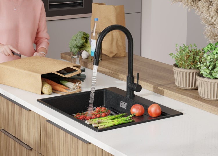 Schwarze Küchenspüle mit Armatur, Gemüse und Person