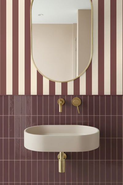 Modernes Badezimmer mit ovalem Waschbecken, goldfarbener Wandarmatur, ovalem Spiegel und Wandgestaltung mit vertikalen Streifen und dunklen Fliesen.