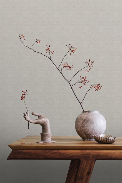 Dekorative Szene mit Zweigen mit roten Beeren in einer Vase, einer Handstatuette und einer Schale auf einem Holztisch.