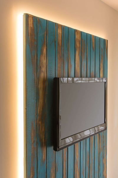 Wandmontierter Fernseher auf blau geöltem Holzpaneel mit integrierter Beleuchtung