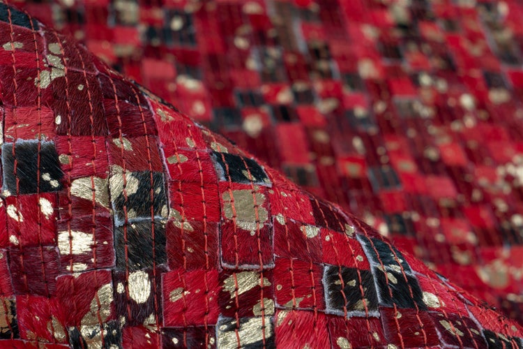 Detailaufnahme eines Patchwork-Teppichs aus Kuhfell in Rot und Schwarz mit goldfarbenen Akzenten.