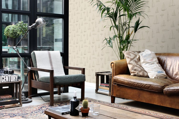 Helles Wohnzimmer mit Vliestapete mit Segelbootmuster, braunem Ledersofa, Holzsessel, Stehlampe und großer Zimmerpflanze.