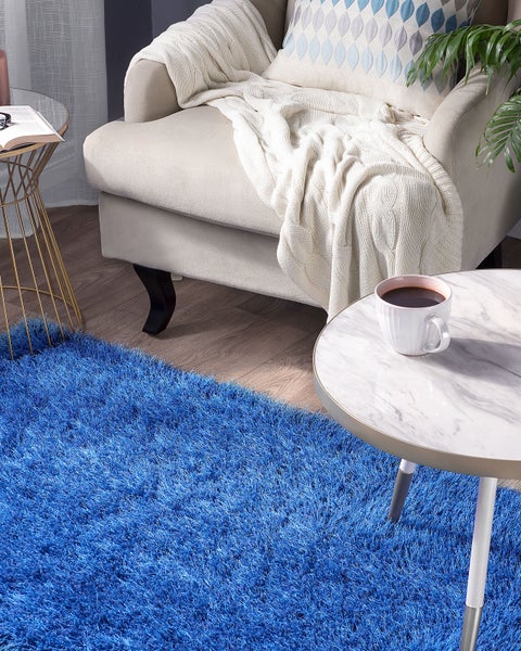 Wohnzimmerszene mit blauem Shaggy-Teppich, Sessel, Couchtisch und Dekoration