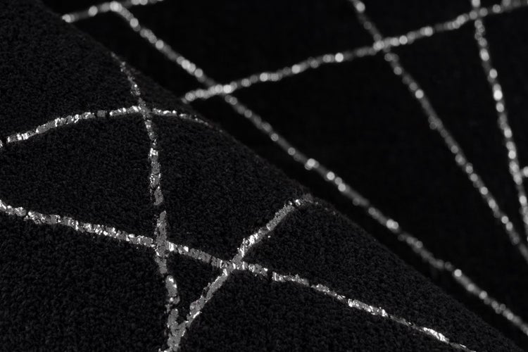 Nahaufnahme eines schwarzen Teppichs mit silbernem geometrischem Linienmuster und weicher Textur.
