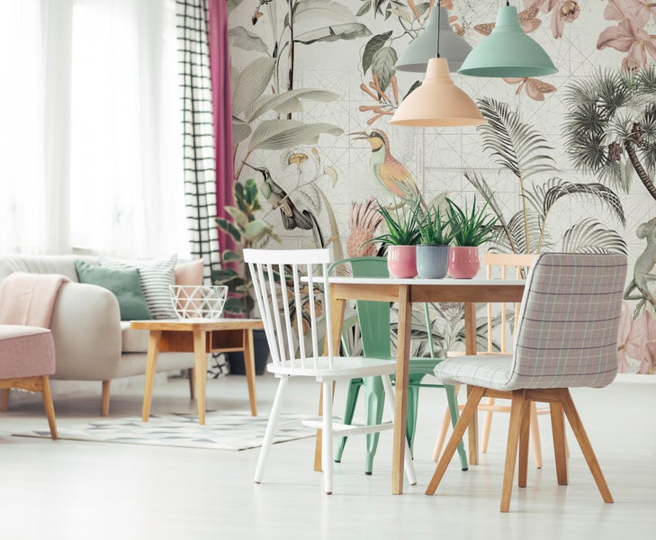 Modernes Esszimmer mit botanischer Mustertapete, rundem Holztisch, verschiedenen Stühlen und Pendelleuchten in einem hellen Wohnraum.