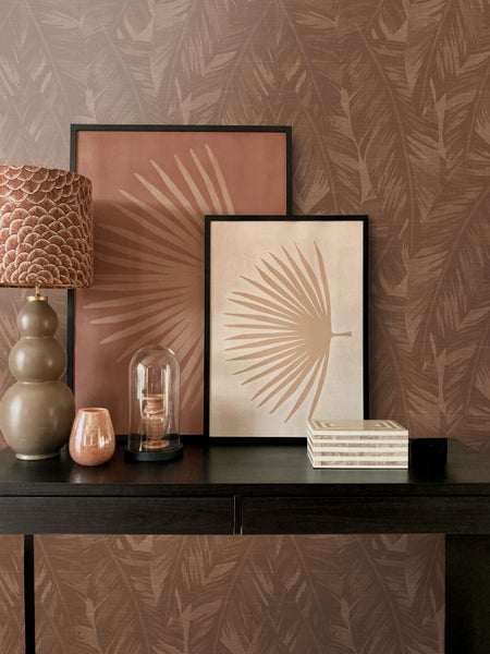 Dekoratives Arrangement mit Lampe, Bildern, Glasglocke und Schatulle auf einem dunklen Holztisch vor einer braunen gemusterten Tapete.