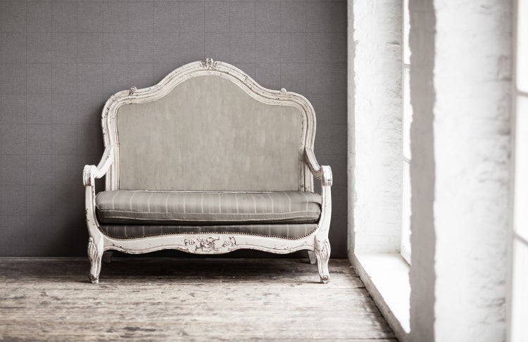 Antikes Sofa mit weißem Rahmen und gestreifter Polsterung vor grauer Wand