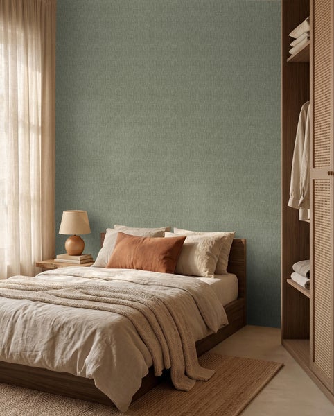 Hell gestaltetes Schlafzimmer mit Bett, Holzschrank und Vliestapete in Leinenoptik. Eine Tischleuchte steht auf dem Nachttisch neben dem Fenster.