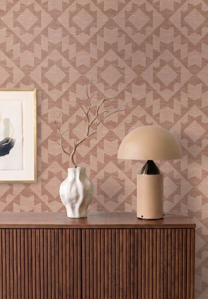 Strukturierte Vliestapete mit geometrischem Rautenmuster an einer Wohnwand mit Sideboard aus Holz, Tischlampe und Blumenvase.